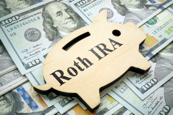 A piggy bank with the words Roth IRA laying on top of a pile of money.