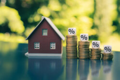 Symbol for decreasing interest rates. Dice with percentage symbols on decreasing high stacks of coins next to a model house.