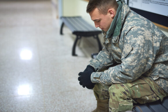 Shot of a young soldier sitting on a bench in the hall of a military academy