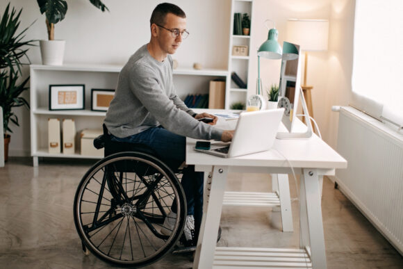 Young man in wheelchair working at a desk on his computer.