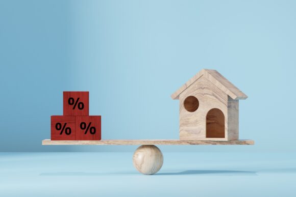 Wooden house balancing on a wooden scale with interest rate blocks on a wooden ball.