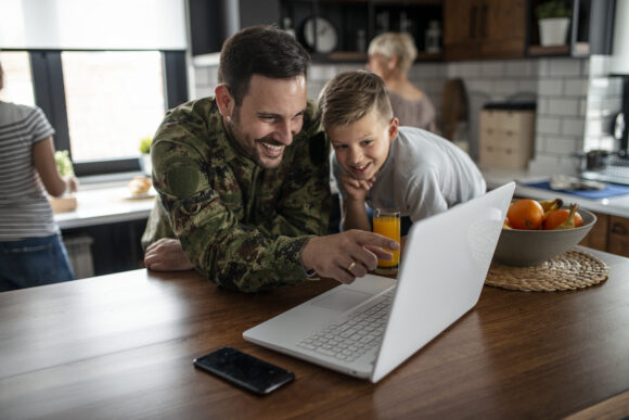 American soldier smiling at computer at home with his family.