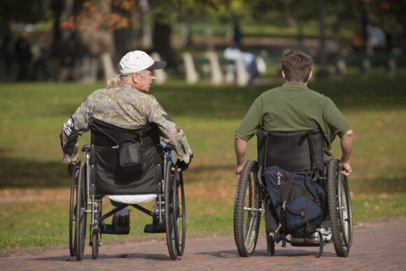 Rear view of two war veterans with spinal cord injuries in wheelchairs in a park