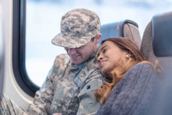 A beautiful woman rests her head on her husband's shoulder as they sit on the train to go home together after his return from the military.