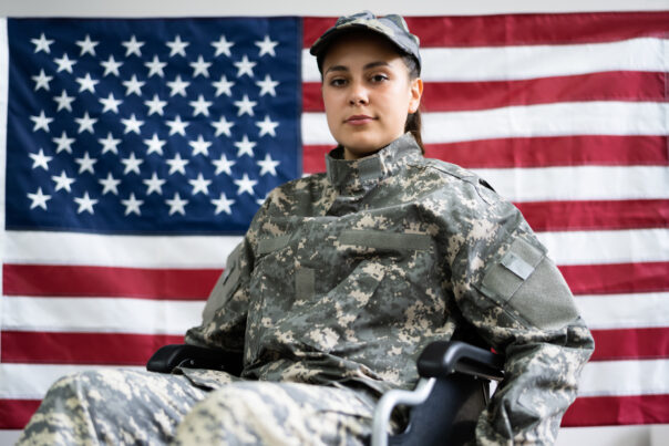 Young female soldier in a wheelchair with an American flag behind her.