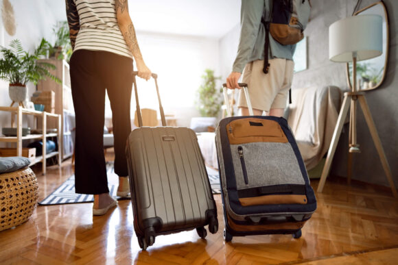 Two adults bringing luggage into a brightly lit living room in an Airbnb